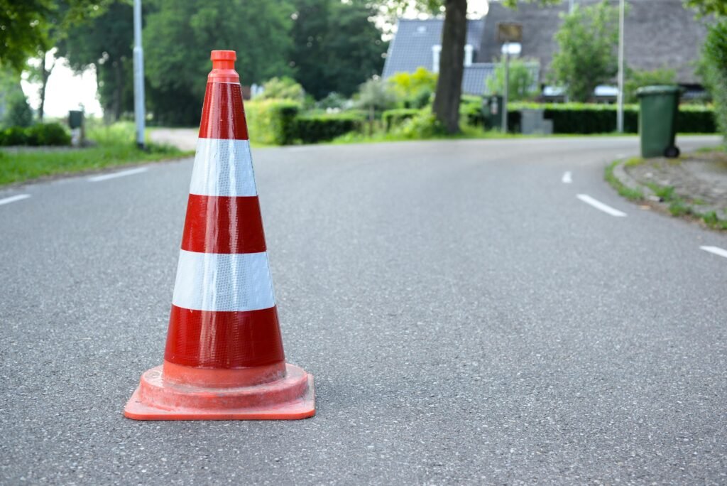 Close-up of a traffic cone on a rural road with trees and houses in the background.