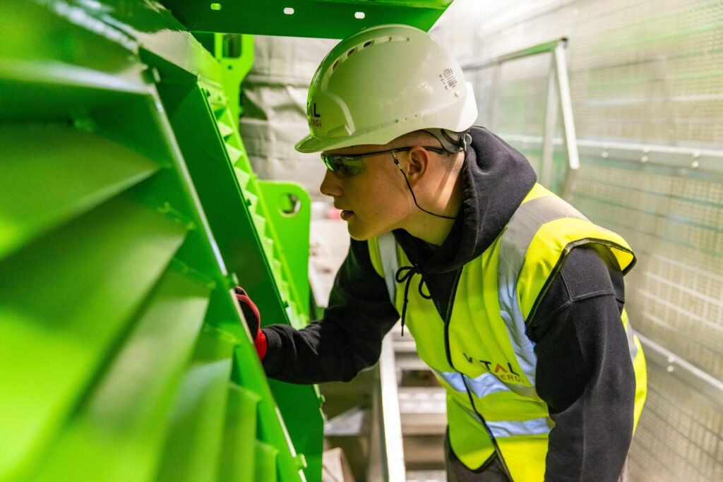 A worker in a safety vest and helmet inspecting industrial machinery.