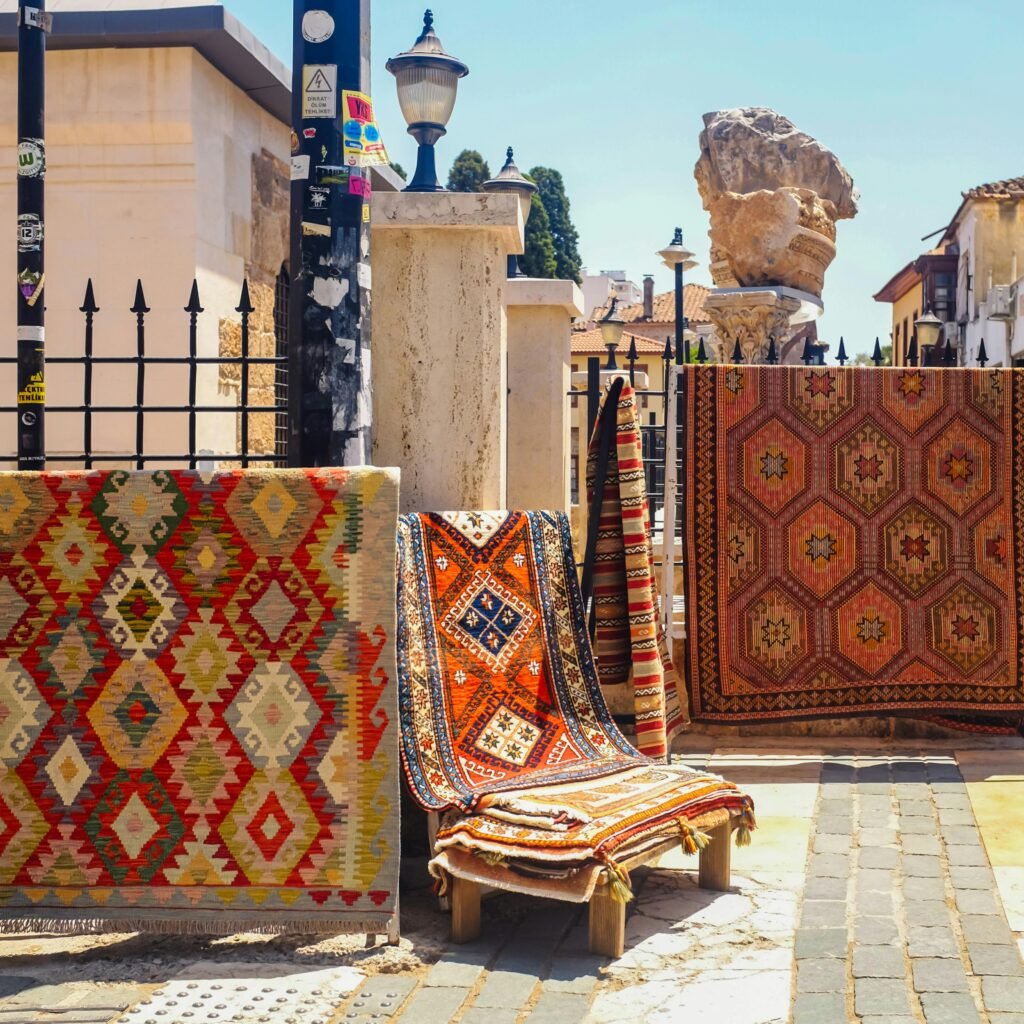 A vibrant display of traditional Turkish Kilim rugs on a sunny street in Antalya, Türkiye.