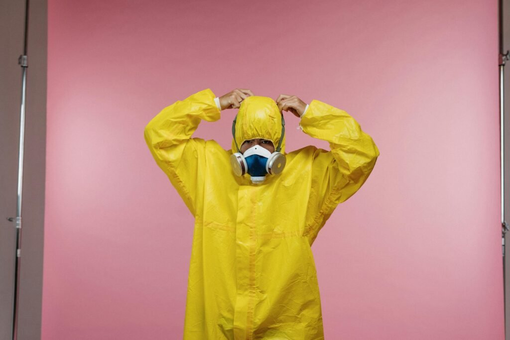 Person wearing a yellow protective suit and respirator against a pink studio background.