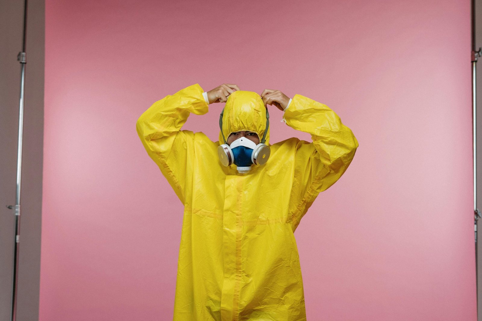 Home Person wearing a yellow protective suit and respirator against a pink studio background.