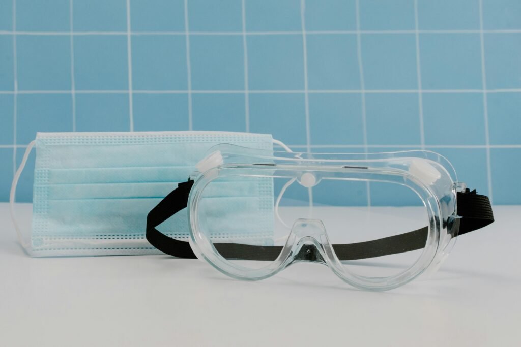 Close-up of protective goggles and a medical face mask against a tiled background.
