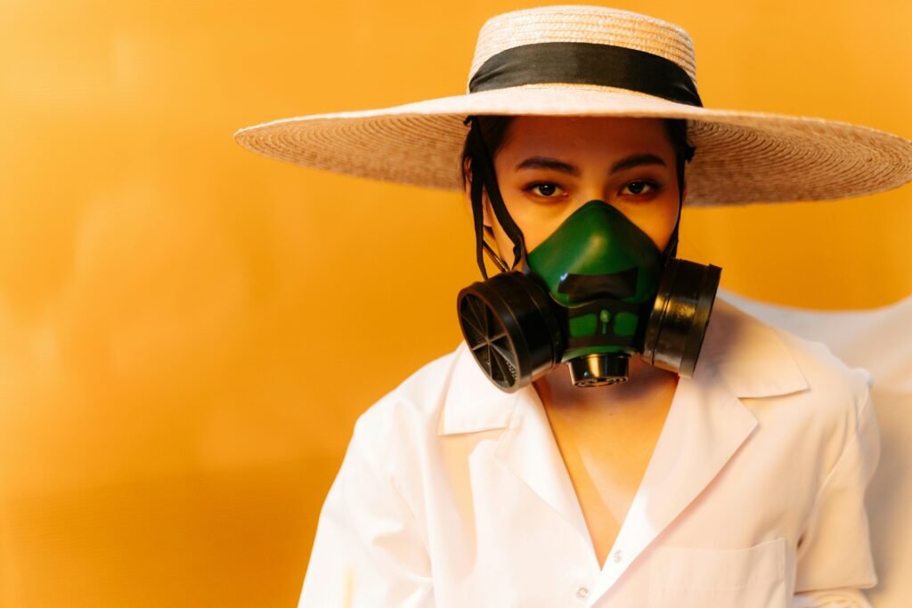 Conceptual portrait of a woman in safety gear with a straw hat and gas mask.