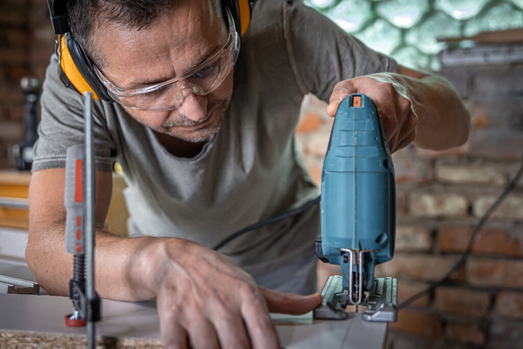 carpenter sawing wood with an electric jigsaw in workshop.