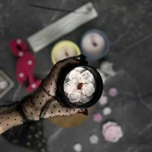 Elegant gloved hand holding a floral scented candle on a dark background, evoking a mysterious mood.