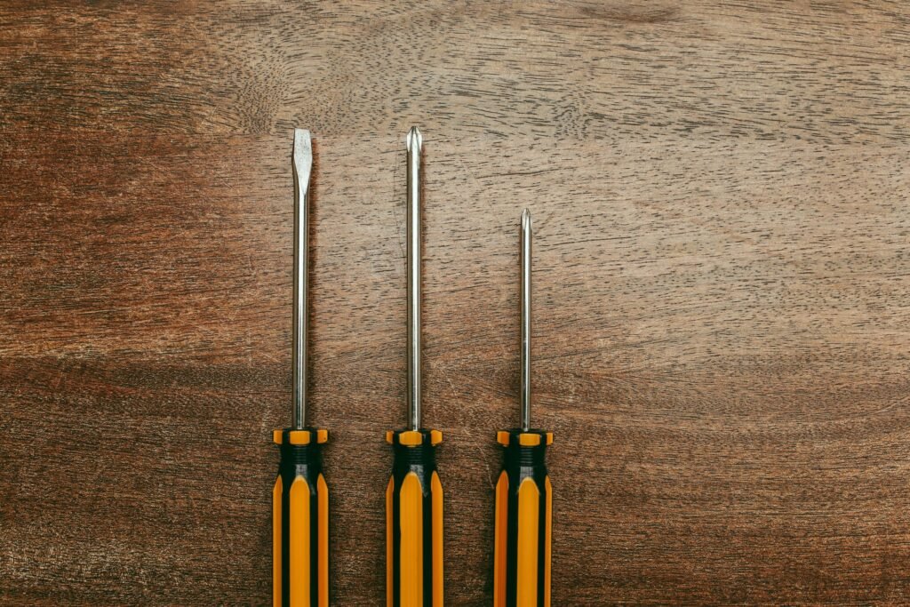 Top view of three screwdrivers laid out on a wooden surface, highlighting repair tools.