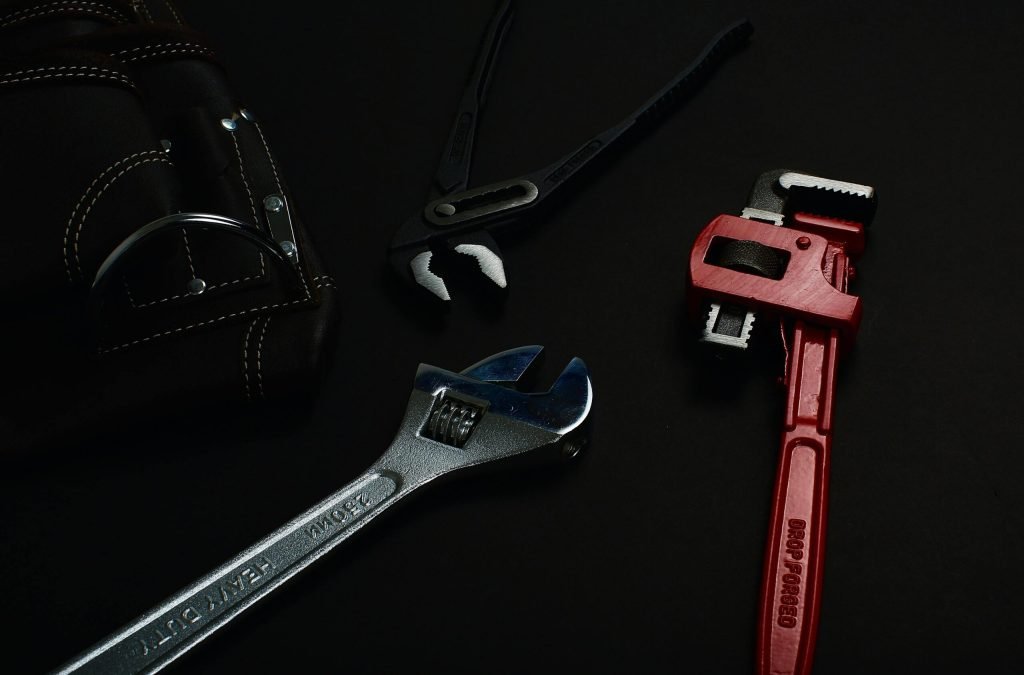 Close-up of various hand tools including wrenches and pliers on a dark surface.