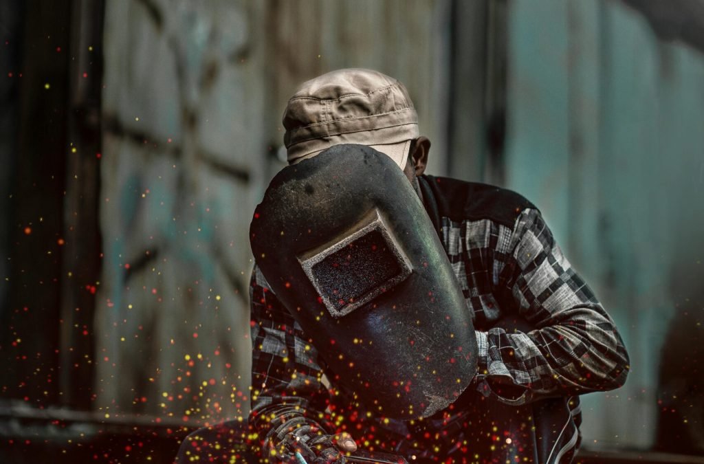 Welder in action with helmet and sparks flying in a gritty industrial setting.