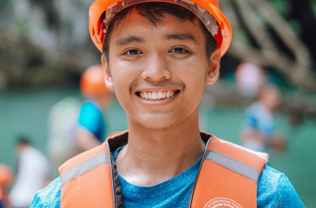 Young man wearing an orange life vest and helmet gives a thumbs-up with a smile.