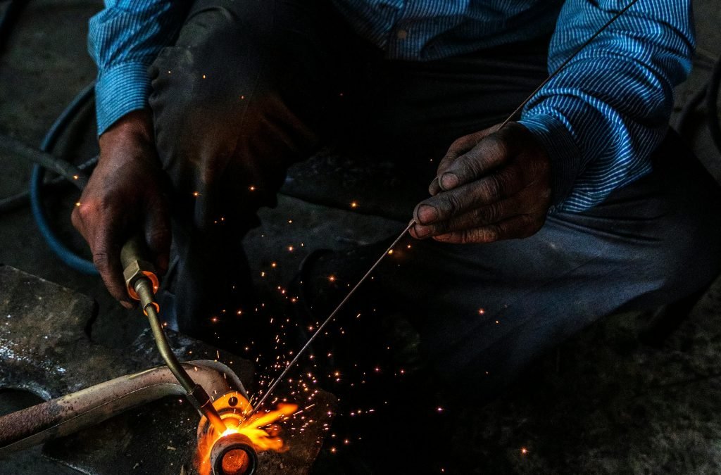 From above of crop unrecognizable workman using welding machine with gas flame while working with metal pipe