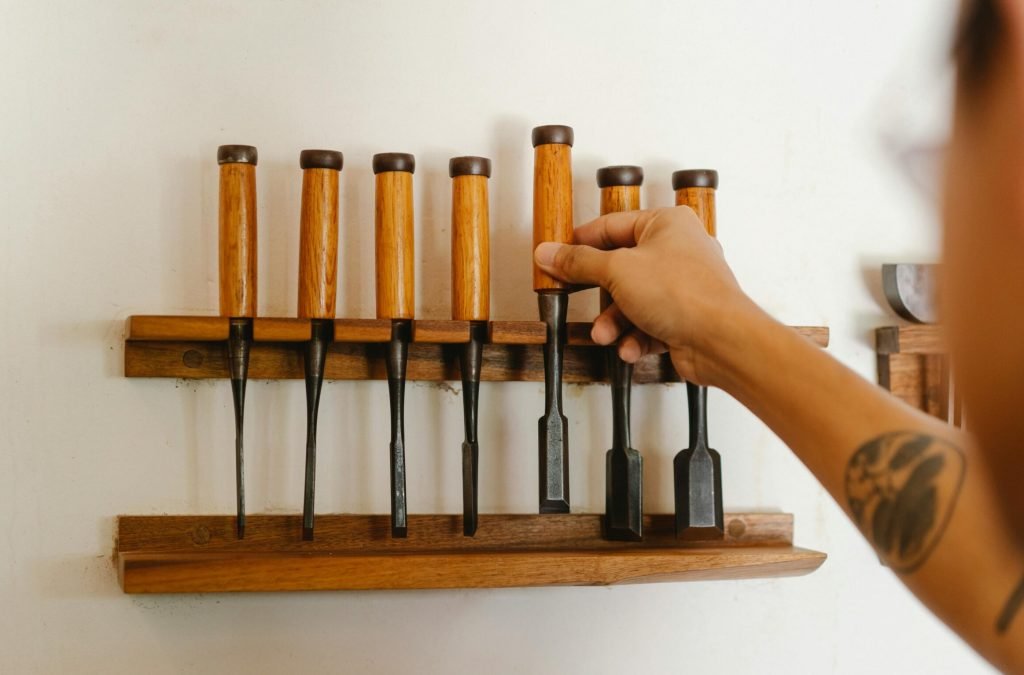 Back view of crop anonymous male taking chisel from set placed on wall in modern joinery studio