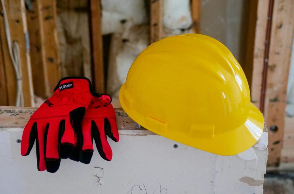 Close-up of a yellow hard hat and red gloves on a construction site, symbolizing safety and work.